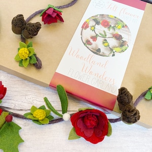 May include: A craft kit for making a felt flower garland. The kit includes felt pieces in red, green, and brown, as well as a length of twine. The box is labelled "Woodland Wonders Flower Garland" and "Felt Flower Craft Kit".