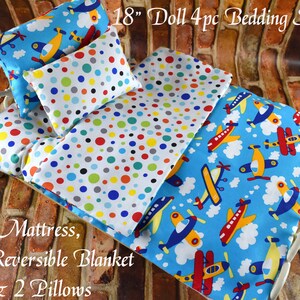 May include: 18" doll bedding set with a reversible blanket featuring a white background with colorful polka dots and a blue background with airplanes. The set also includes two pillows with a white background and colorful polka dots.