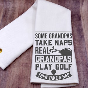 May include: White kitchen towel with a gray graphic that reads "Some Grandpas Take Naps Real Grandpas Play Golf Then Take A Nap". The graphic includes a golf bag and golf clubs.