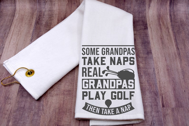 May include: White kitchen towel with a gray graphic that reads "Some Grandpas Take Naps Real Grandpas Play Golf Then Take A Nap". The graphic includes a golf bag and golf clubs.