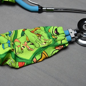 May include: A green stethoscope cover with a Teenage Mutant Ninja Turtles print. The cover is wrapped around a blue and silver stethoscope.