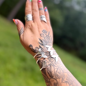 May include: Three silver-toned metal bracelets, each featuring a distinct whale tail or fluke design. The bracelets are open-ended, allowing for adjustment around the wrist. The metal has a smooth, polished finish that reflects light clearly.