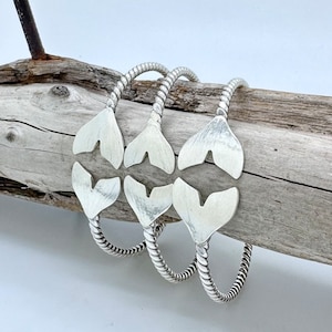 May include: Three silver bracelets with a twisted rope design and a heart-shaped charm. The charms are open at the top and have a textured finish.