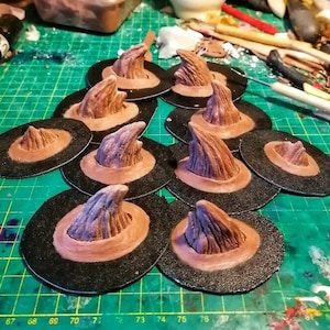 May include: A collection of ten brown witch hat toppers with a pointed, textured design. The toppers are arranged on a green cutting mat with black markings.