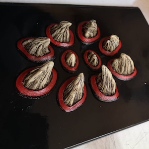 May include: A black background with ten beige, textured, 3D spikes with red rings around each one. The spikes are arranged in a circular pattern.