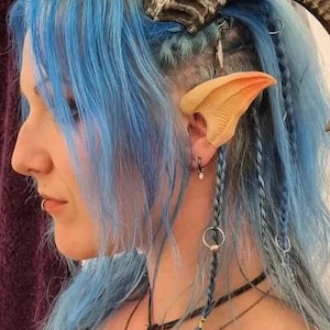 Puede incluir: Una persona con el pelo azul que lleva un par de orejas de elfo. Las orejas están hechas de un material marrón claro y están sujetas a las orejas de la persona con un pequeño anillo de metal.