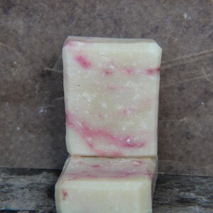 Puede incluir: Dos barras de jabón hechas a mano, una encima de la otra. La barra superior es blanca con remolinos rosas. La barra inferior es blanca con remolinos rosas y es parcialmente visible.