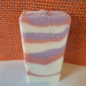 Puede incluir: Una pastilla de jabón con un patrón de remolino blanco, rosa y morado.