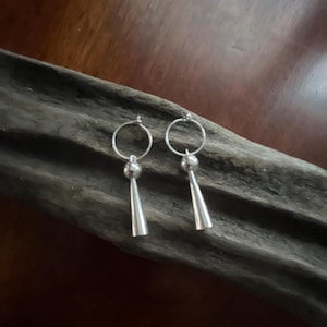 May include: A pair of silver hoop earrings with a cone-shaped pendant hanging from each hoop.