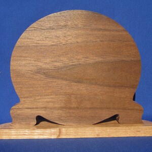 May include: A wooden decorative piece with a rounded top and a rectangular base. The top is made of a darker wood, while the base is a lighter wood. Two black, pointed accents are cut into the base.