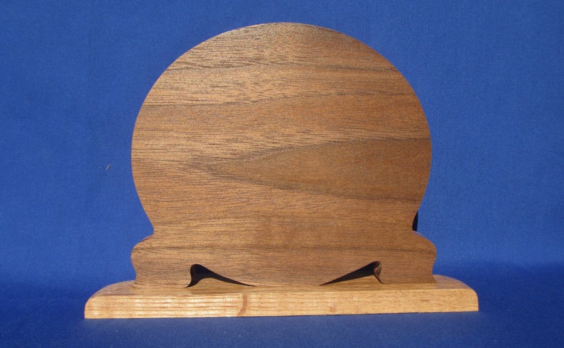 May include: A wooden decorative piece with a rounded top and a rectangular base. The top is made of a darker wood, while the base is a lighter wood. Two black, pointed accents are cut into the base.