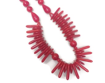 Peut inclure: Un collier composé de perles rouge vif et de composants allongés en forme de bâtonnets. Le design comprend deux rangs de perles rondes menant à une section centrale composée de nombreux bâtonnets rouges fins et rayonnants.