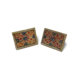 May include: A pair of rectangular earrings featuring a floral design. The earrings have a beige border and a red, blue, and yellow floral pattern. They are set against a white background.
