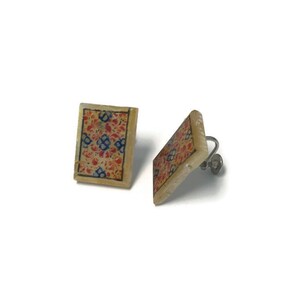May include: A pair of square earrings featuring a cream-coloured base and a floral design in red, blue, and gold. The earrings have a clip-on mechanism and are set against a white backdrop.