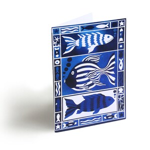 May include: A blue and white greeting card with a stylized design of three fish. The fish are outlined in white and have a blue and white striped pattern. The card has a white background and a blue border.