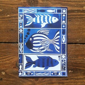 May include: Three stylized fish in a blue and white pattern on a card. The fish are outlined in white and have black eyes. The card has a blue background with white waves and stars.