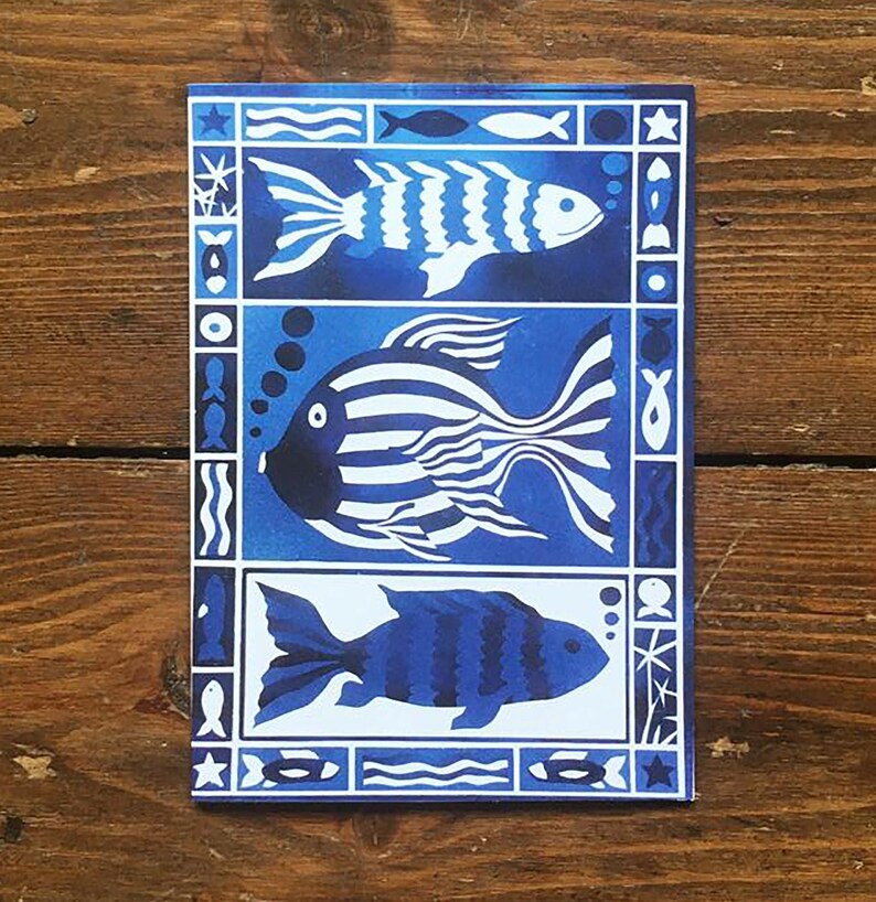 May include: Three stylized fish in a blue and white pattern on a card. The fish are outlined in white and have black eyes. The card has a blue background with white waves and stars.