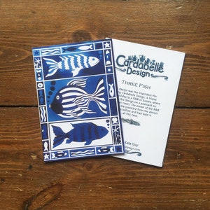 May include: A blue and white greeting card with a design of three stylized fish. The card has a white border and the text "Three Fish" and "Cardabelle Design" in black.