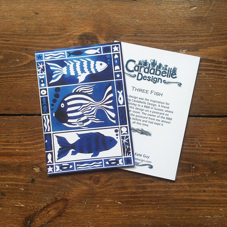 May include: A blue and white greeting card with a design of three stylized fish. The card has a white border and the text "Three Fish" and "Cardabelle Design" in black.