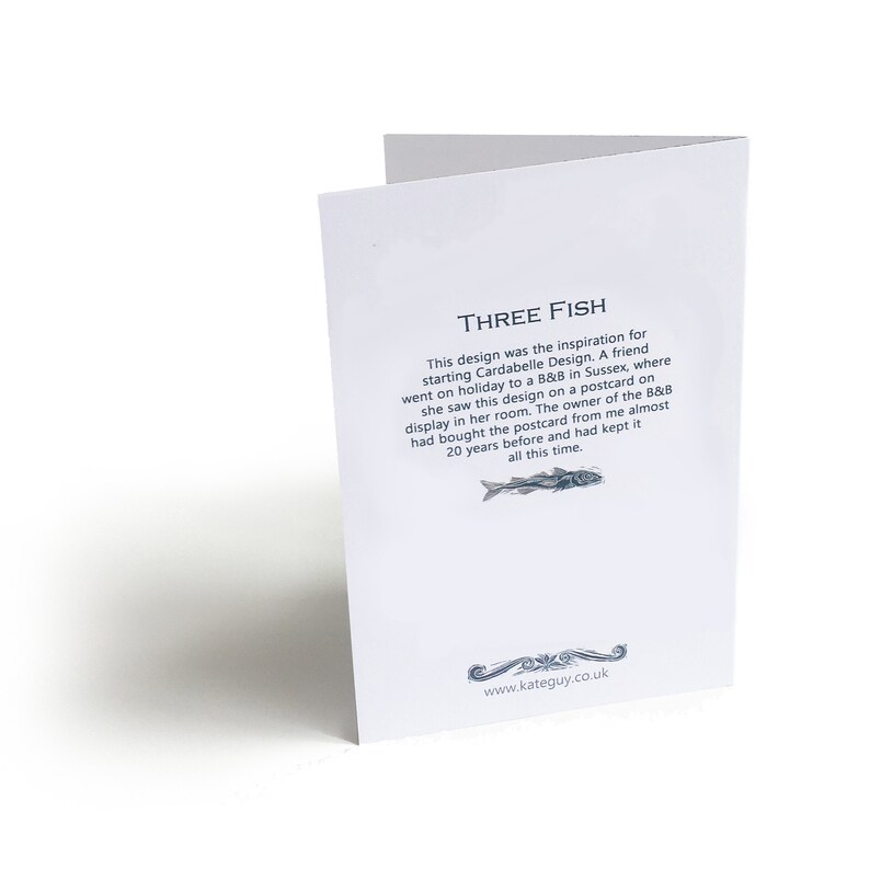 May include: A white card with the text "THREE FISH" and a description of how the design was inspired by a postcard seen at a B&B in Sussex, England. The card also includes the website address "www.kateguy.co.uk".