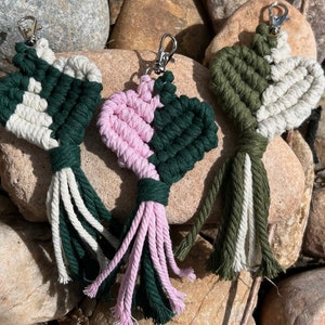 May include: Three handmade macrame heart keychains with tassels. One is green and white, one is pink and green, and one is olive green and white.