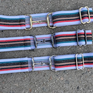 May include: Three white elastic belts with colorful stripes and a metal buckle. The belts have a red, black, and teal stripe pattern.