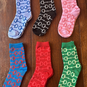 May include: Six pairs of colorful socks with a repeating pattern of equestrian stirrups. The socks are in shades of blue, black, pink, red, and green.