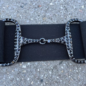 May include: Black elastic belt with a silver-tone buckle encrusted with black rhinestones.