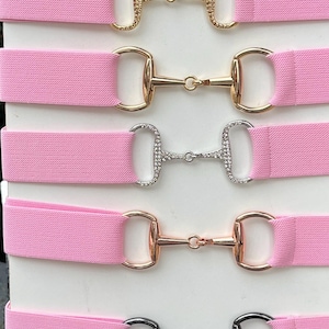 May include: Seven pink elastic belts with different colored metal horse bit buckles. The buckles are adorned with clear or black rhinestones.