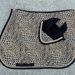 Peut inclure: Un tapis de selle imprimé léopard brun et noir avec un tapis de selle en maille noir et blanc en dessous. Le tapis de selle a une bordure noire avec des strass dorés.