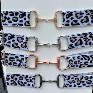 May include: Four different styles of leopard print elastic hair ties with metal snappers. The snappers are gold, silver, rose gold, and black.