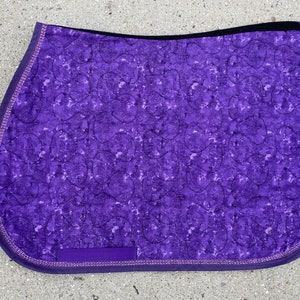May include: Purple quilted saddle pad with a swirl pattern and a black and purple trim.