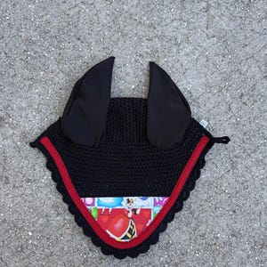 May include: Black equestrian fly bonnet with black ear coverings and a red trim. The bonnet features a colorful fabric panel with an illustration of the Queen of Hearts from Alice in Wonderland.