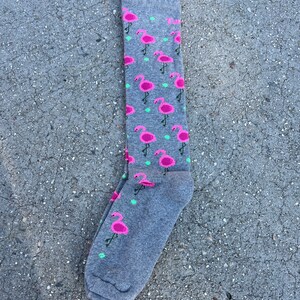 May include: Gray knee-high socks with a pink flamingo pattern. The socks have a small green leaf design.