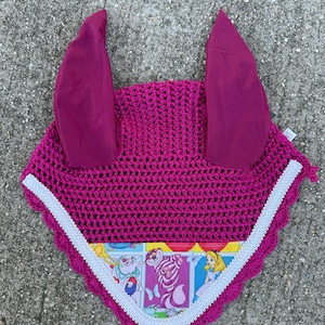 May include: A magenta crochet horse bonnet with matching ear covers. The bonnet features a white scalloped trim and a colorful Alice in Wonderland print. The ear covers are made of a solid magenta fabric.