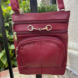 May include: A burgundy leather crossbody bag with three zippered compartments and a silver horse bit accent.