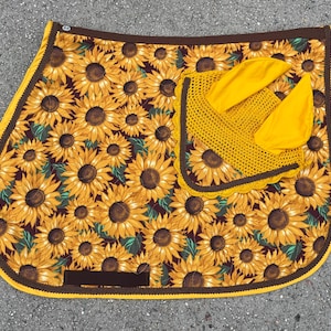 May include: A horse saddle pad and matching ear bonnet set. The saddle pad features a sunflower pattern with a brown border and yellow trim. The ear bonnet is yellow and crocheted.