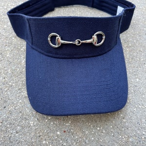 May include: A navy blue visor with a silver horse bit detail.