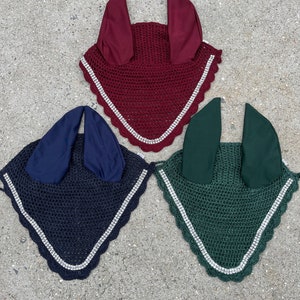 May include: Three horse fly hoods in different colors: burgundy, navy blue, and forest green. Each hood has a white rhinestone trim around the edge.