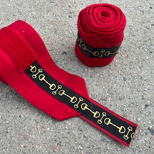 May include: Red horse leg wraps with black and gold trim featuring a repeating snaffle bit design.