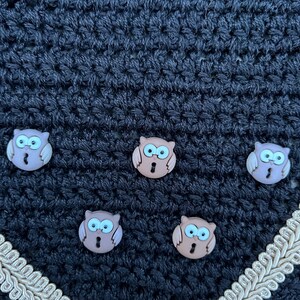 May include: Black crocheted fabric with five brown owl buttons. The fabric has a gold trim around the bottom edge.
