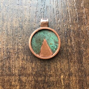 Può includere: Un ciondolo in rame con patina verde e un triangolo in rame al centro.