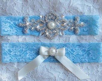 Pode incluir: Uma liga de noiva azul claro com um laço de cetim branco e um grande enfeite de strass e pérolas.