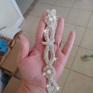 K&ouml;nnte beinhalten: Ein silbernes Strass-Haarband mit zwei Perlenakzenten. Das Haarband ist mit einem zarten, filigranen Muster verziert.