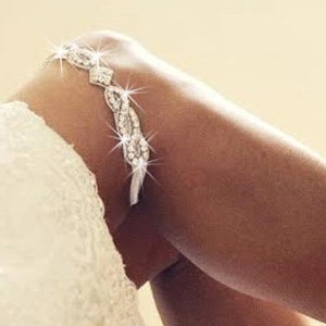May include: A white bridal garter with a silver rhinestone embellishment. The garter is made of a delicate lace material and features a sparkling design.