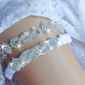 May include: A white satin garter with a silver rhinestone embellishment. The garter is decorated with a row of sparkling rhinestones.