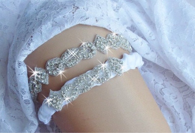 May include: A white satin garter with a silver rhinestone embellishment. The garter is decorated with a row of sparkling rhinestones.