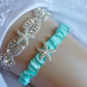 K&ouml;nnte beinhalten: Ein t&uuml;rkisblaues Satin-Strumpfband mit einer Strass-Seestern-Verzierung. Ein zweites Strumpfband mit einem Strass-Seestern und Perlen-Design ist ebenfalls sichtbar.