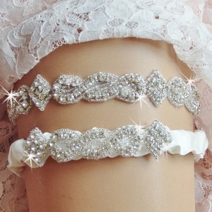 May include: A white satin garter with a silver rhinestone embellishment. The garter has a delicate, floral design and is perfect for a wedding or special occasion.