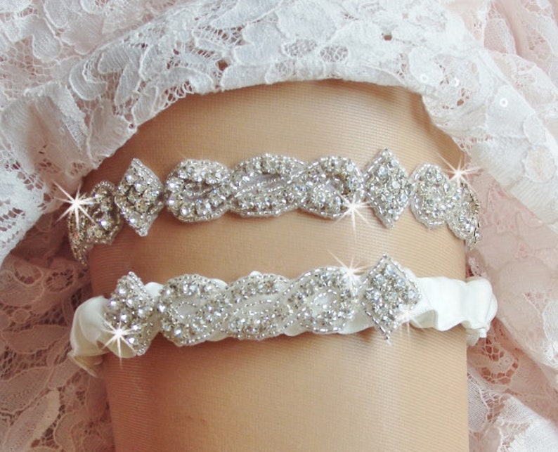 May include: A white satin garter with a silver rhinestone embellishment. The garter has a delicate, floral design and is perfect for a wedding or special occasion.